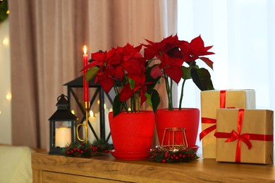 Photo of Potted poinsettias, burning candles and festive decor on dresser in room. Christmas traditional flower