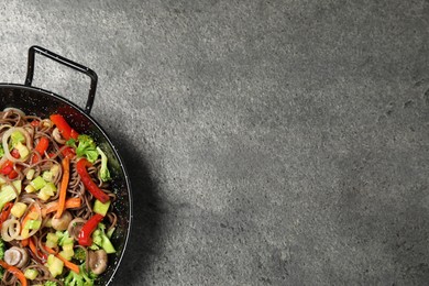 Stir fried noodles with mushrooms and vegetables in wok on grey table, top view. Space for text