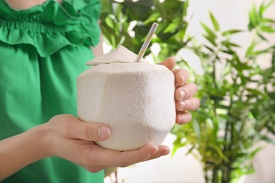 Photo of Woman with fresh coconut drink in nut on green plants background, closeup