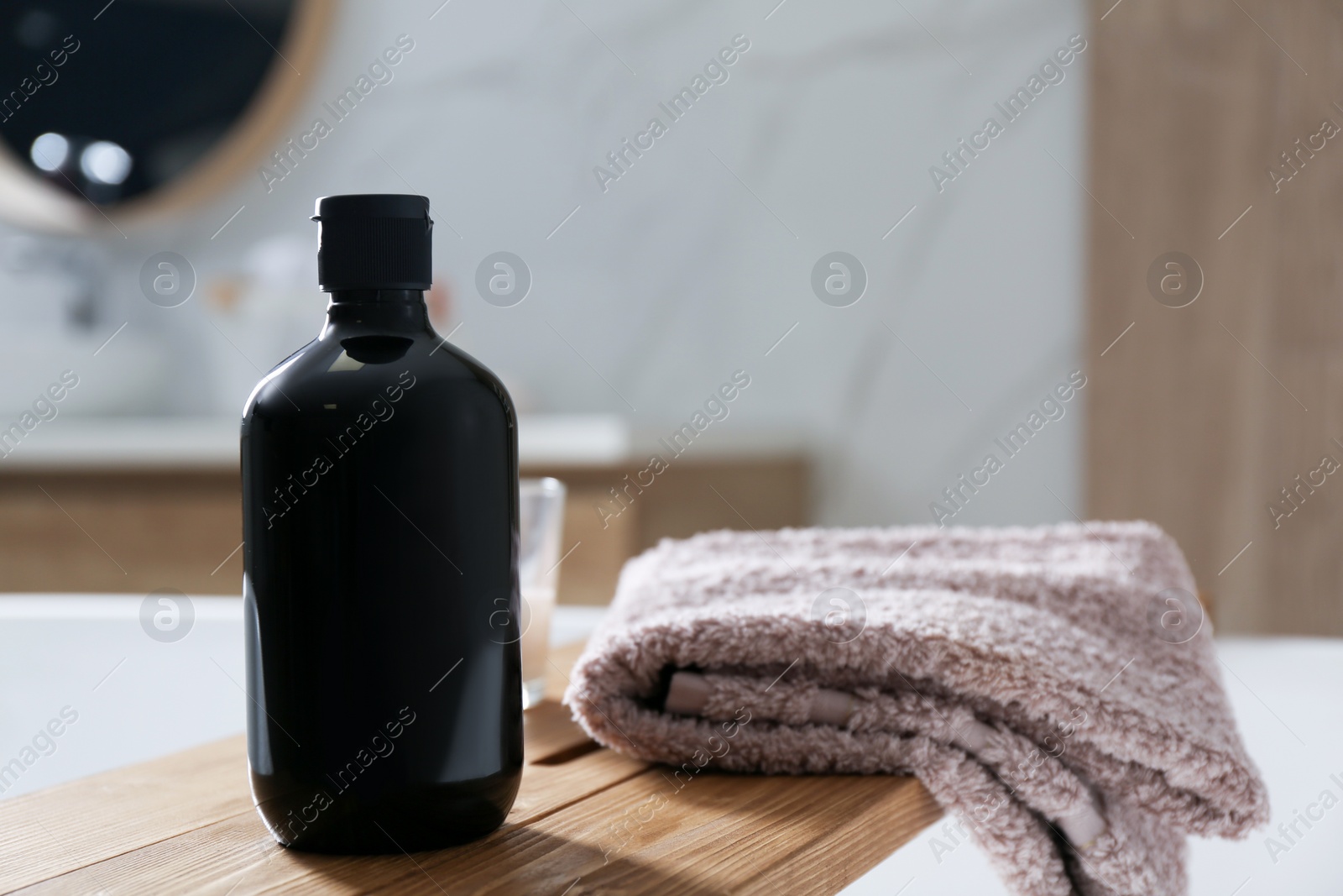 Photo of Wooden bath tray with shower gel and fresh towel on tub indoors