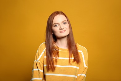 Photo of Candid portrait of happy young woman with charming smile and gorgeous red hair on yellow background