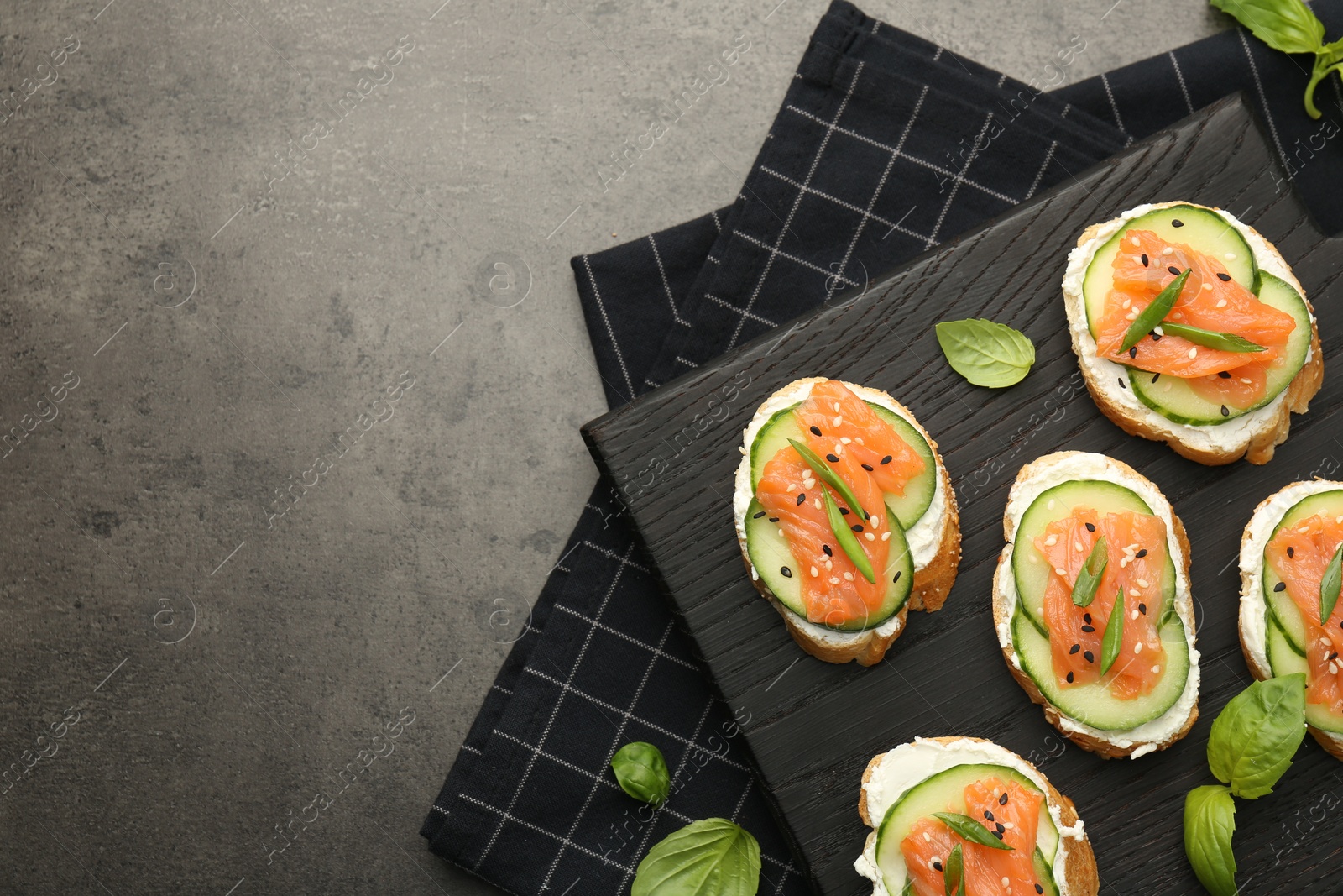 Photo of Tasty canapes with salmon, cucumber and cream cheese on grey table, top view. Space for text