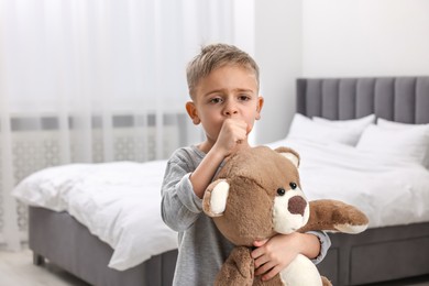 Photo of Sick boy with teddy bear coughing at home