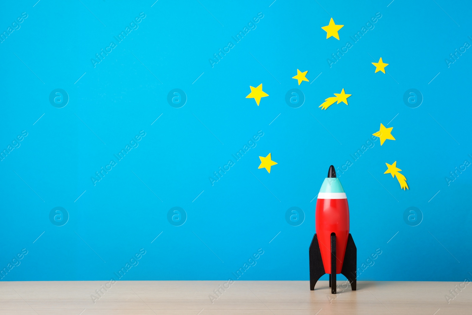 Photo of Bright toy rocket on wooden desk. Space for text