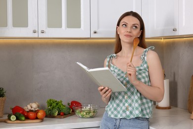 Happy woman with recipe book in kitchen, space for text