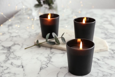 Photo of Burning candles and green branch with fairy lights on marble table