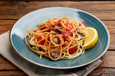 Photo of Delicious pasta with anchovies, tomatoes and parmesan cheese on wooden table, closeup