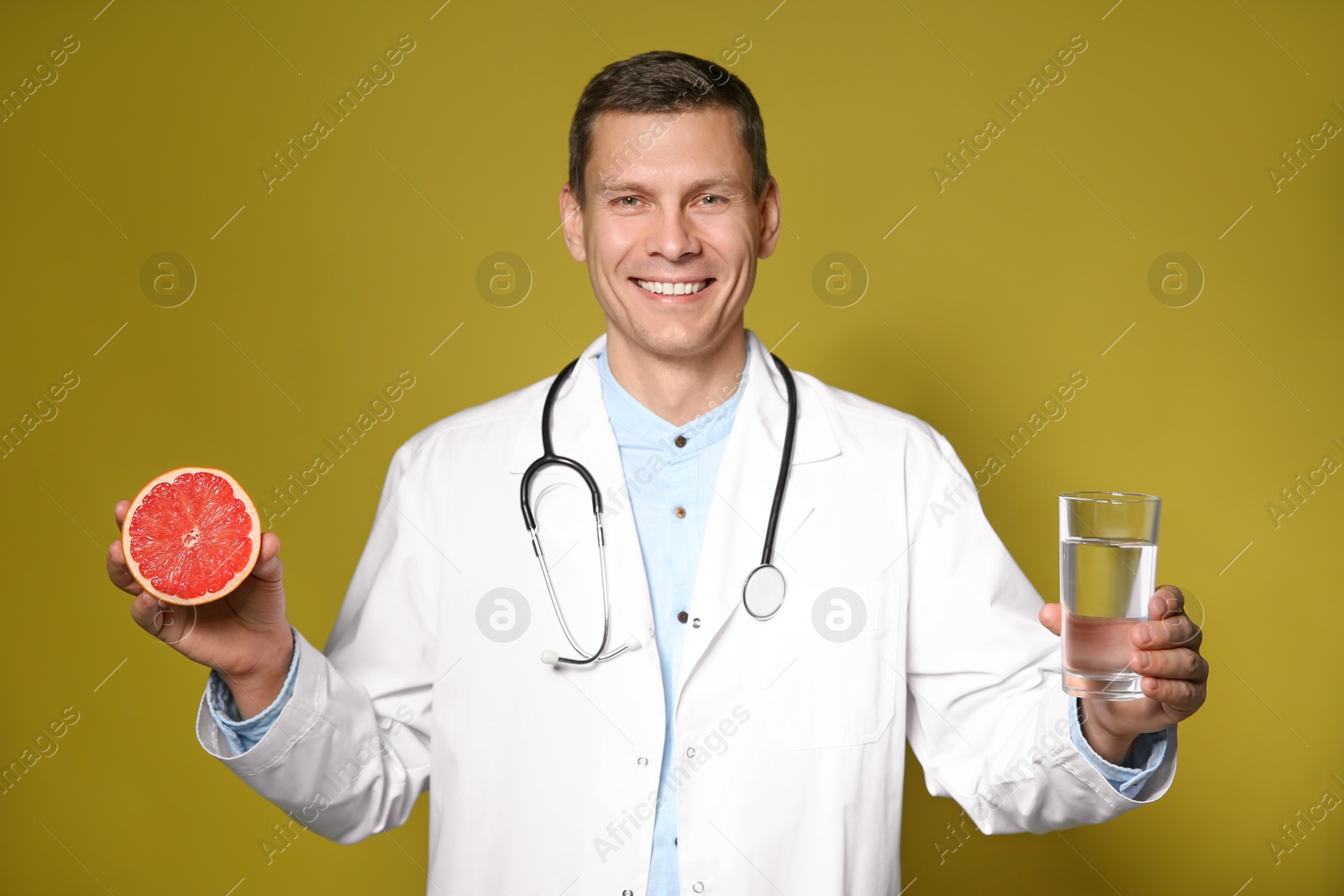 Photo of Nutritionist holding glass of pure water and ripe grapefruit on yellow background