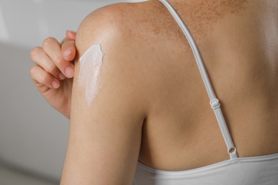 Photo of Woman applying body cream onto shoulder on blurred background, closeup