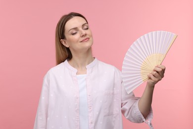 Photo of Beautiful woman waving hand fan to cool herself on pink background