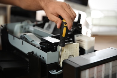 Photo of Repairman with screwdriver fixing modern printer, closeup