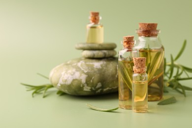 Aromatic essential oils in bottles, rosemary and pebble stones on green background