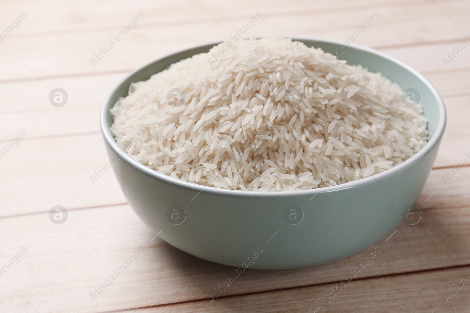 Photo of Raw basmati rice in bowl on white wooden table, closeup