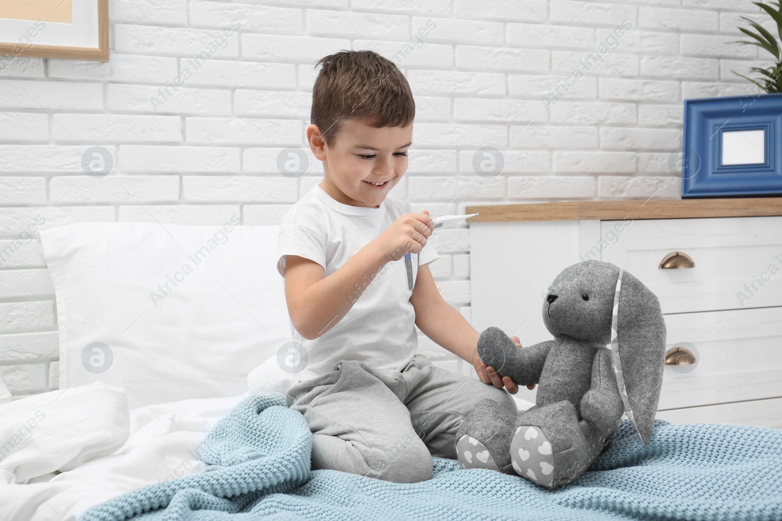 Photo of Cute child playing doctor with stuffed toy on bed in hospital ward