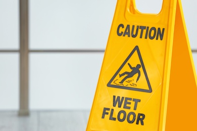 Photo of Safety sign with phrase Caution wet floor on blurred background. Cleaning service