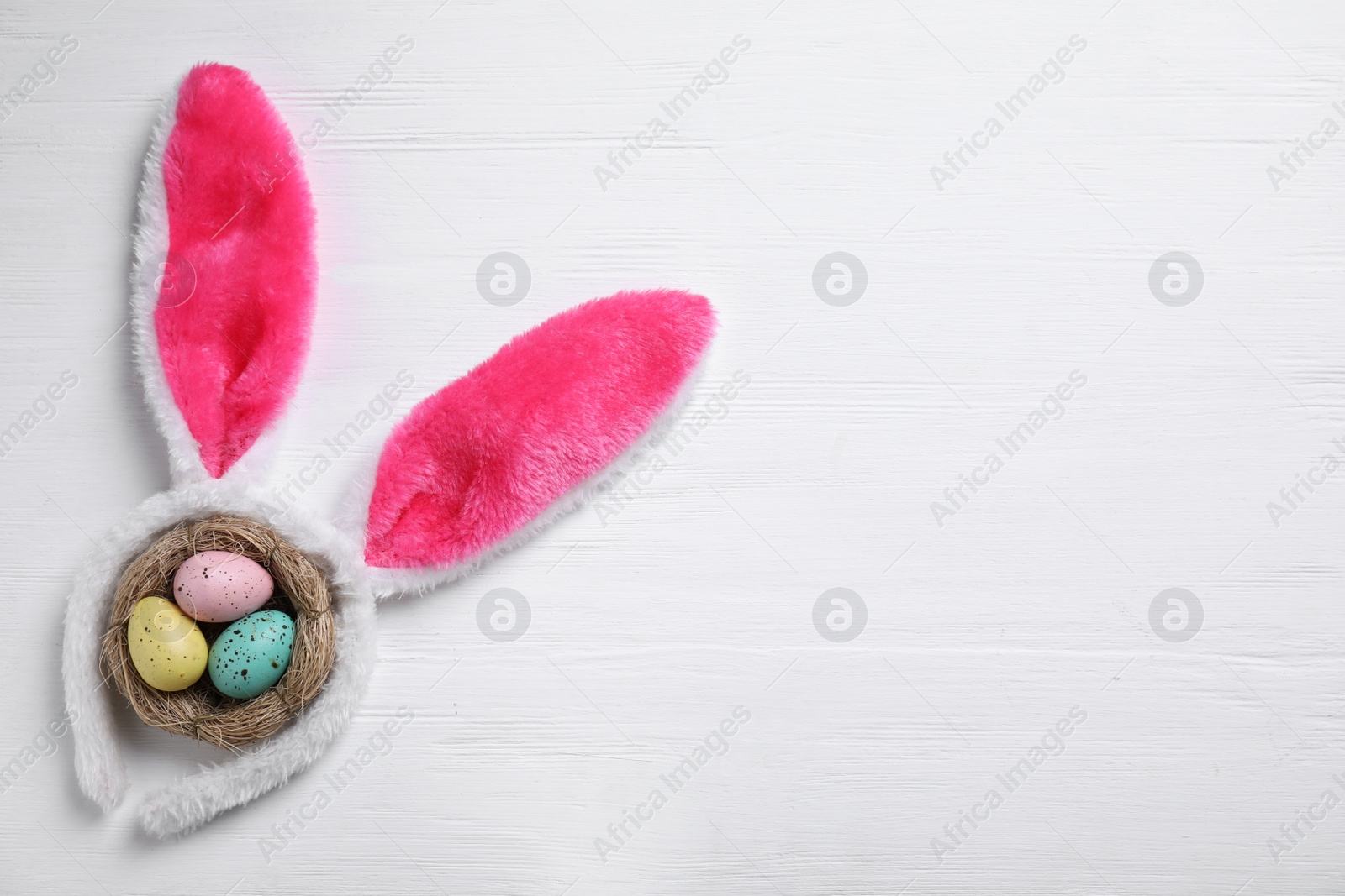 Photo of Headband with bunny ears, painted eggs and space for text on white wooden background, flat lay. Easter holiday