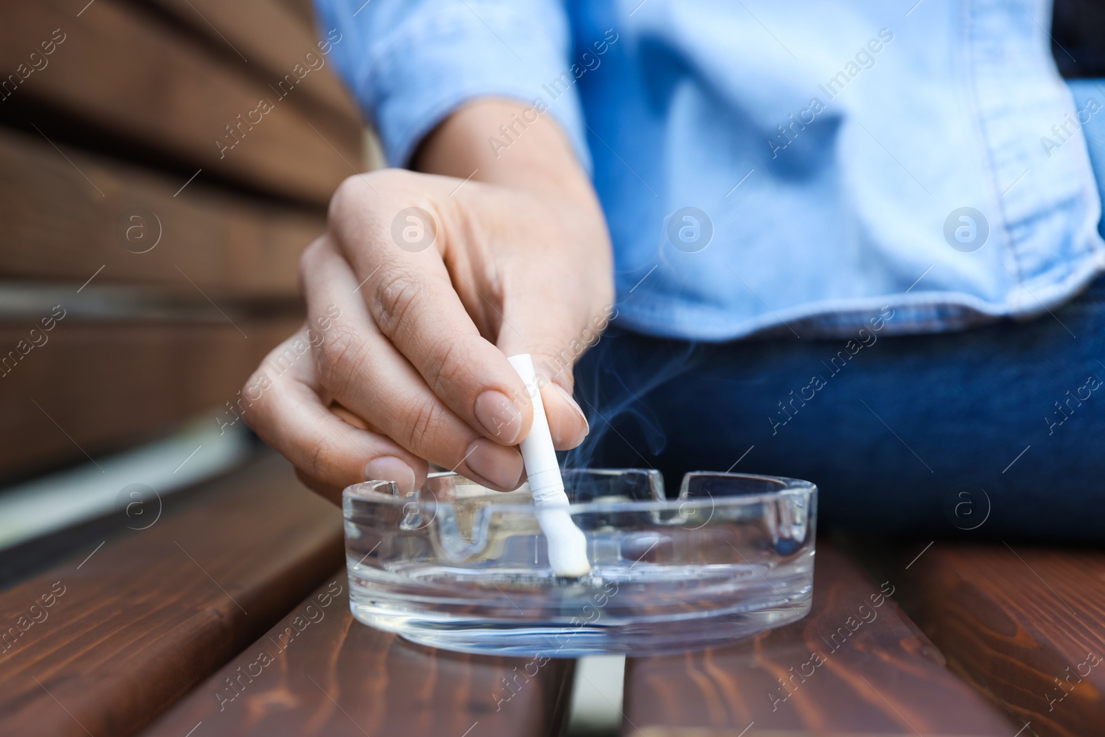 Photo of Woman putting out cigarette in ashtray on wooden bench, closeup