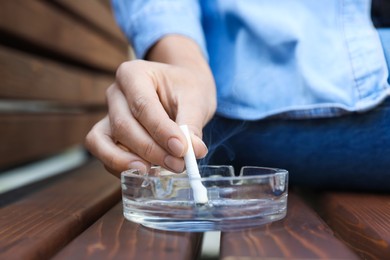 Photo of Woman putting out cigarette in ashtray on wooden bench, closeup
