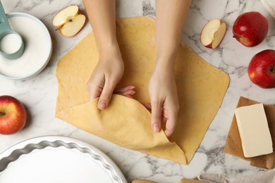 Photo of Woman with raw dough for traditional English apple pie at white marble table, top view