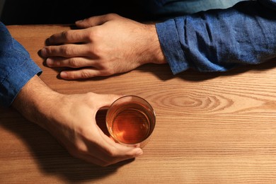 Addicted man with glass of alcoholic drink at wooden table, top view