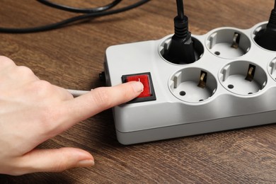 Photo of Woman pressing button of power strip on wooden floor, closeup. Electrician's equipment