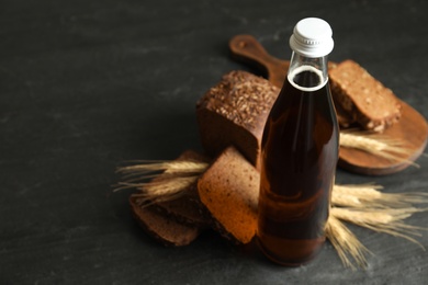 Photo of Bottle of delicious fresh kvass, spikelets and bread on grey table, closeup. Space for text