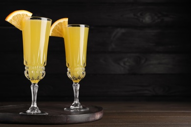 Photo of Glasses of Mimosa cocktail with garnish on wooden table. Space for text