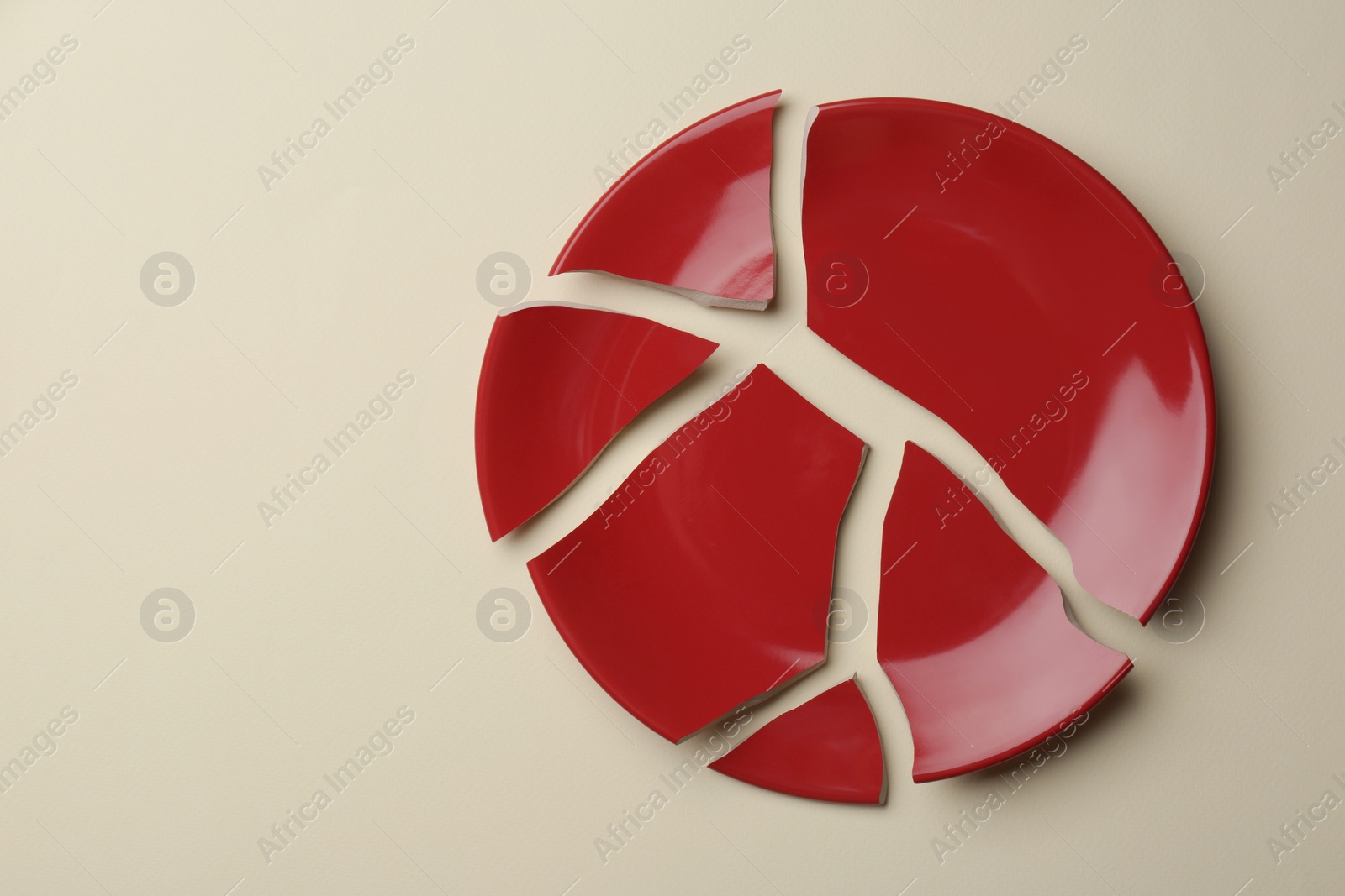 Photo of Pieces of broken red ceramic plate on beige background, top view. Space for text