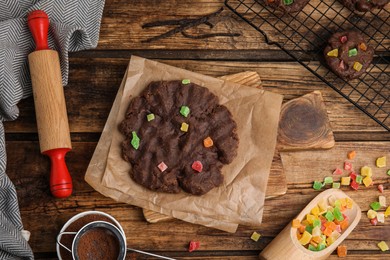 Photo of Unbaked chocolate cookies with candied fruits on wooden table, flat lay