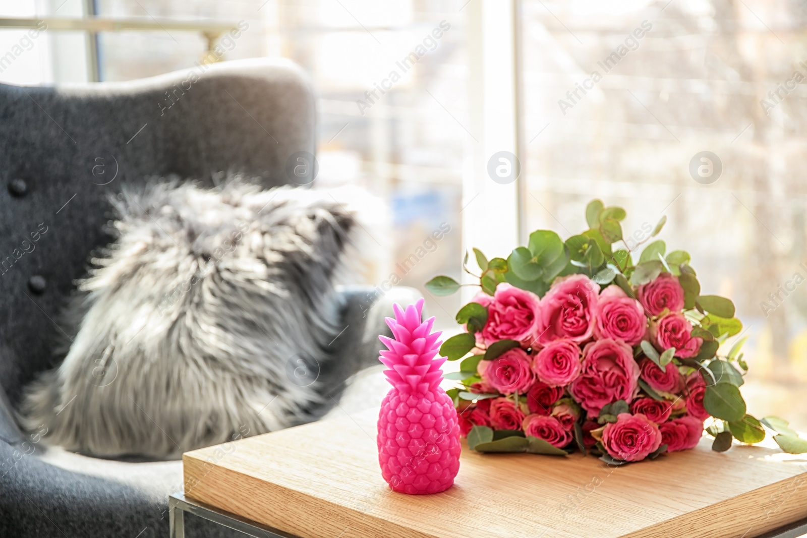 Photo of Pineapple shaped candle and bouquet of flowers on table in room