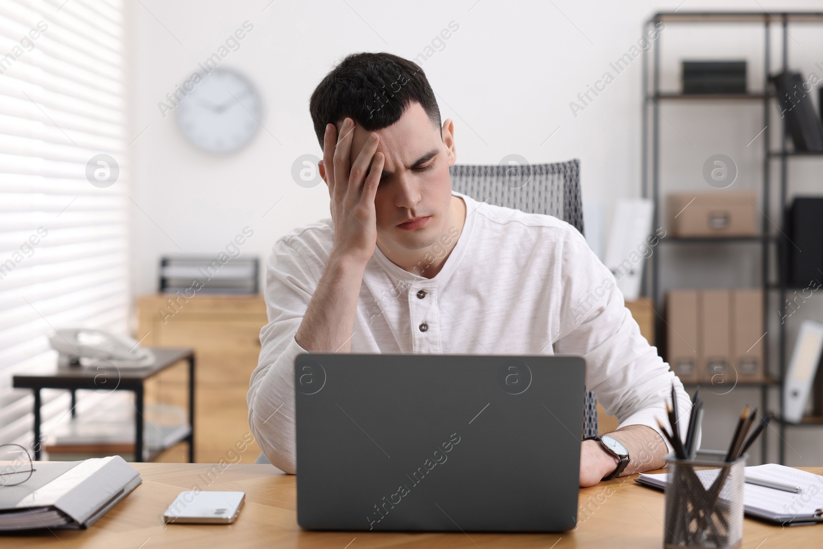 Photo of Young man suffering from headache at workplace in office