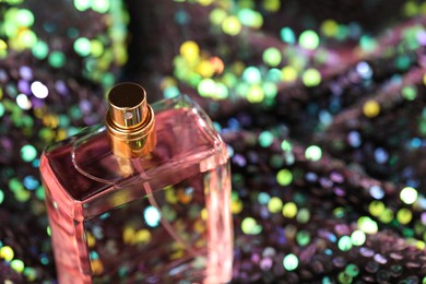 Photo of Luxury perfume in bottle on fabric with colorful sequins, closeup