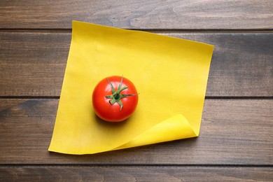 Photo of Fresh ripe tomato and waxed napkin on wooden table, top view
