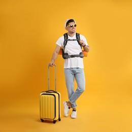 Male tourist with travel backpack and suitcase on yellow background