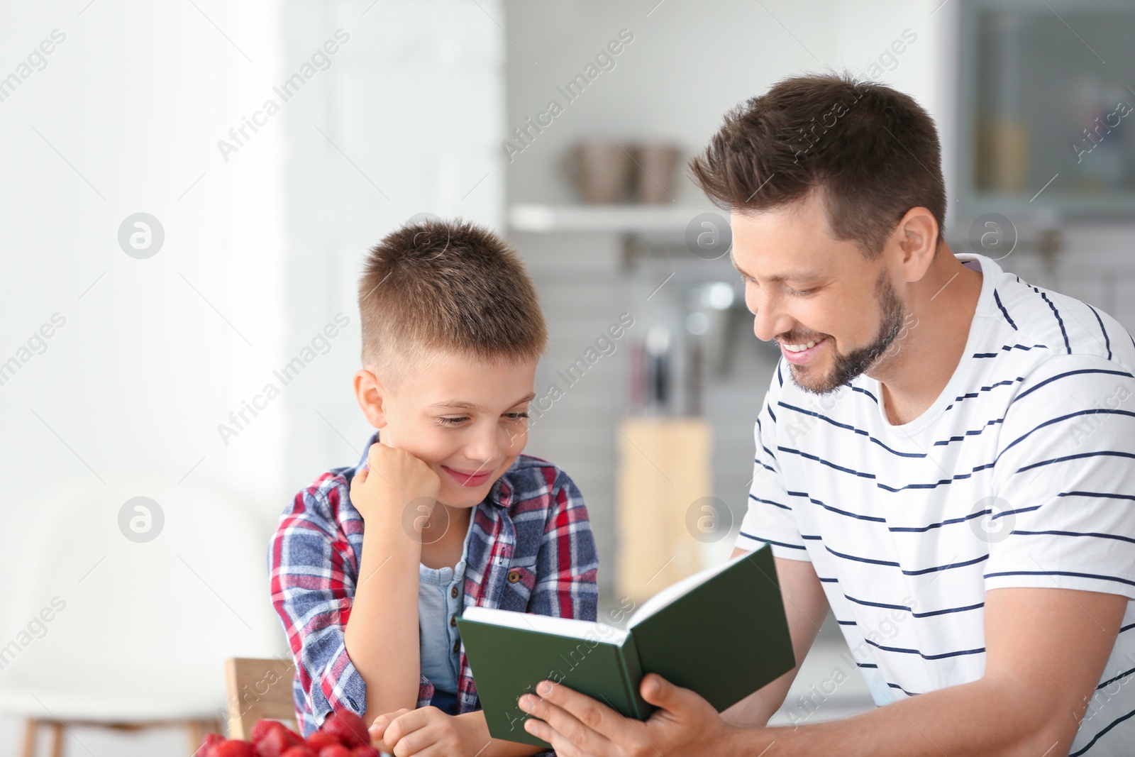 Photo of Dad and son reading interesting book in kitchen