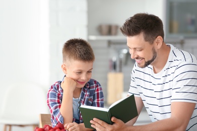 Dad and son reading interesting book in kitchen