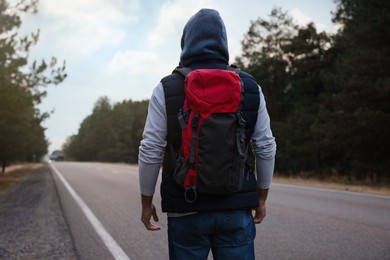 Man with backpack on road near forest, back view