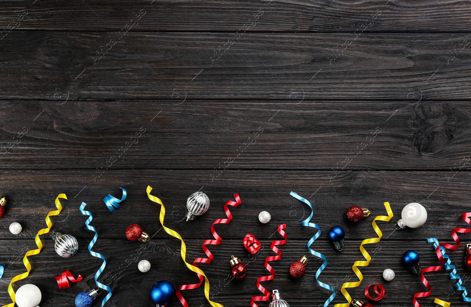 Photo of Colorful serpentine streamers and Christmas balls on black wooden background, flat lay. Space for text