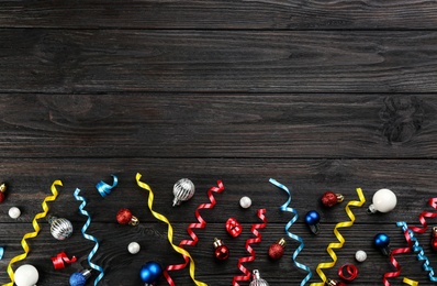 Colorful serpentine streamers and Christmas balls on black wooden background, flat lay. Space for text
