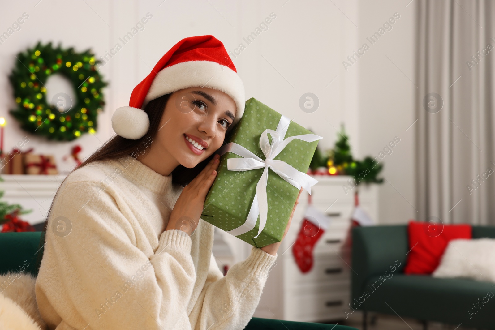 Photo of Happy young woman in Santa hat with Christmas gift at home, space for text