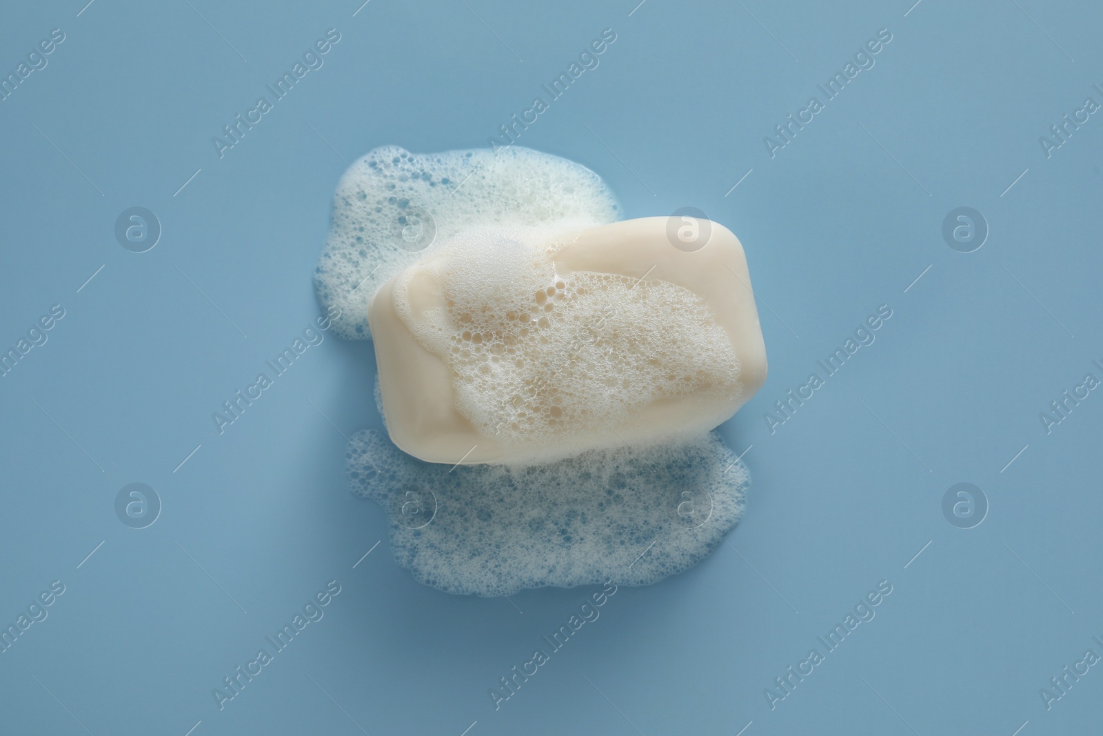 Photo of Soap bar with fluffy foam on light blue background, top view