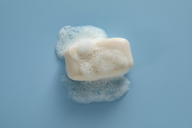 Soap bar with fluffy foam on light blue background, top view