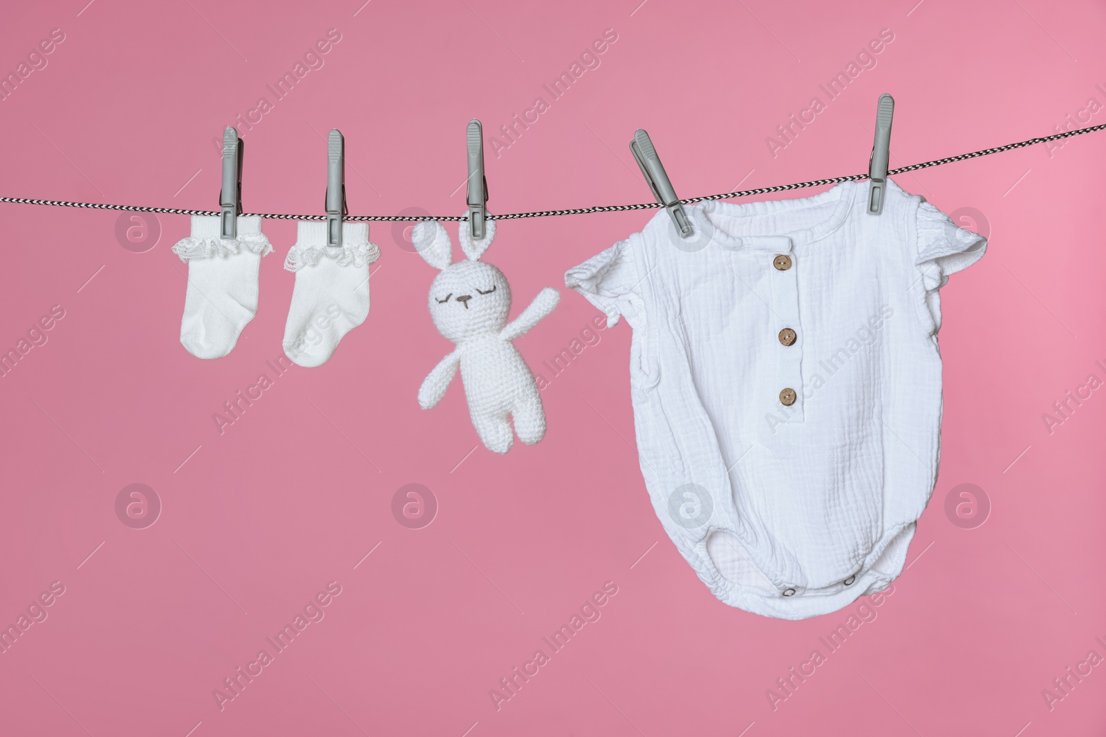 Photo of Different baby clothes and bunny toy drying on laundry line against pink background
