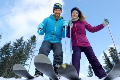 Photo of Happy couple with ski equipment outdoors, view from below. Winter vacation