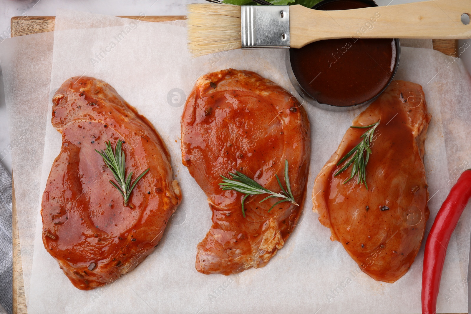 Photo of Raw marinated meat, rosemary and basting brush on table, flat lay