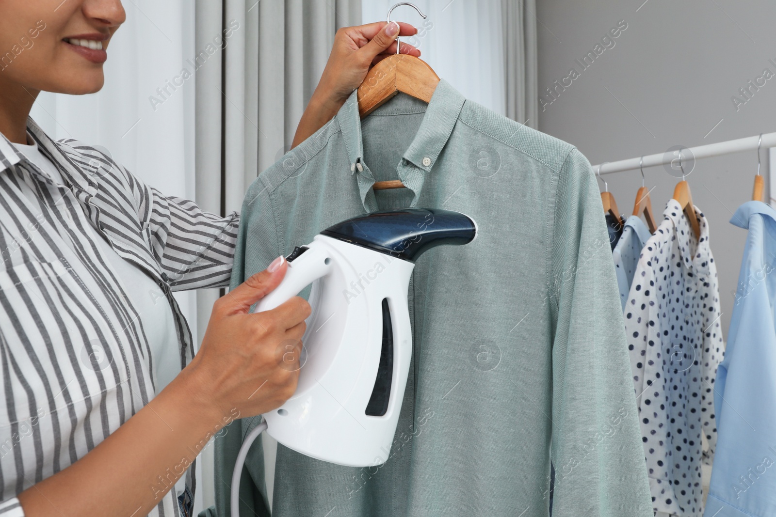 Photo of Woman steaming shirt on hanger at home, closeup