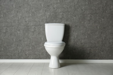 Photo of New toilet bowl near grey wall indoors
