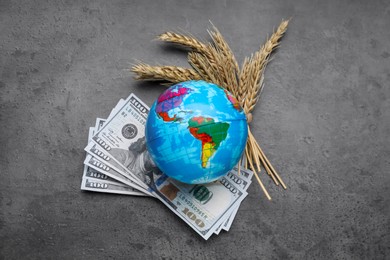 Photo of Globe, ears of wheat and banknotes on grey table, flat lay. Import and export concept