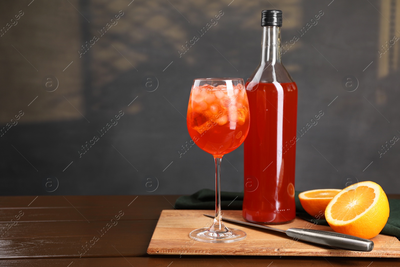 Photo of Aperol spritz cocktail and ice cubes in glass and bottle on wooden table, space for text