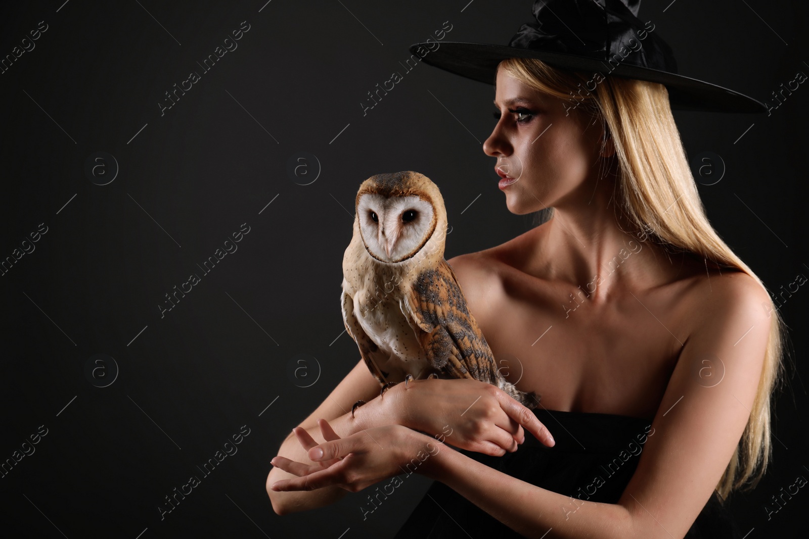 Photo of Witch in black hat with owl on dark background. Scary fantasy character